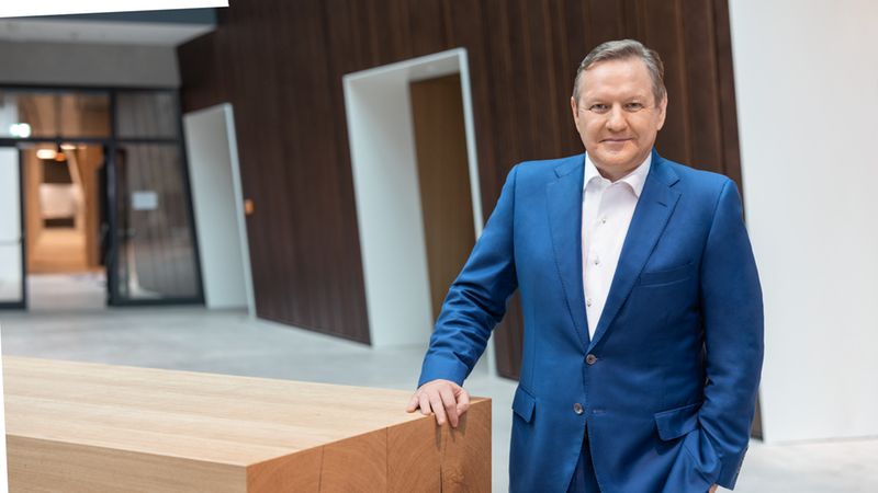 Ein Mann in einem blauen Anzug steht in einem modernen Bürogebäude neben einem Holztisch.
