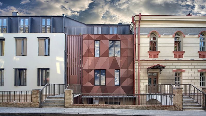 Eine moderne HPL-Gebäudefassade mit geometrischen Mustern zwischen zwei traditionellen Gebäuden.
