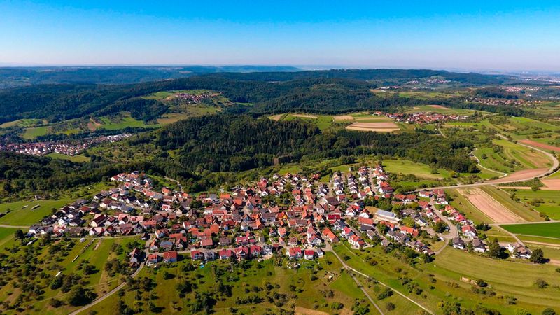 Eine malerische Luftaufnahme eines Dorfes, umgeben von grünen Feldern und Wäldern.