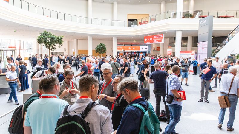 Eine große Messehalle voller Besucher, die sich unterhalten und umsehen.
