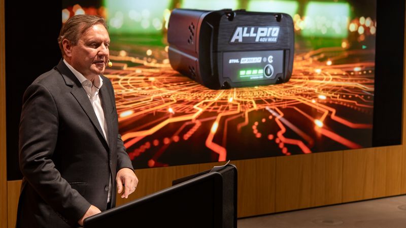 Ein Mann hält eine Präsentation über eine neue Akku-Innovation, die auf einem Bildschirm im Hintergrund zu sehen ist.