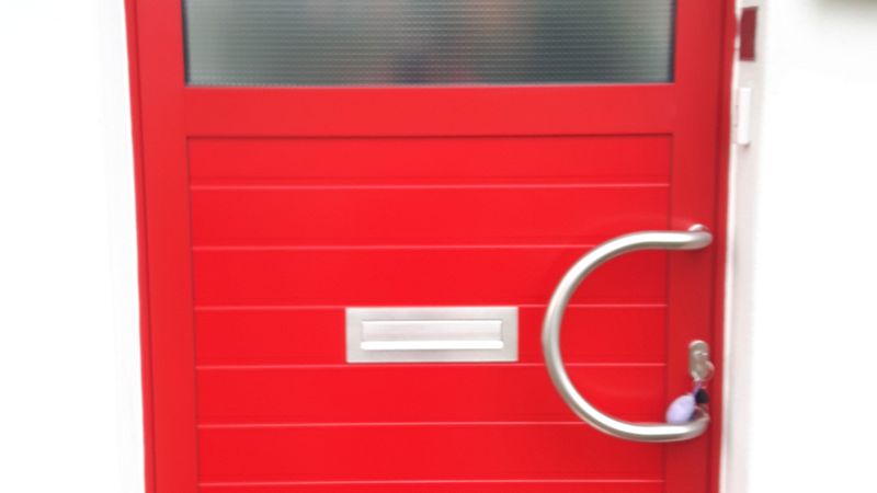 Eine leuchtend rote Haustür mit einem großen, runden Türgriff und einem Briefschlitz in der Mitte.