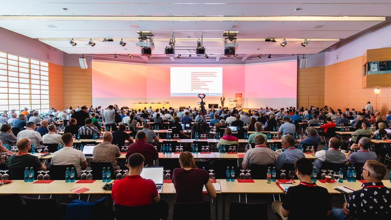Ein großer Konferenzraum voller Teilnehmer, die einer Präsentation folgen.