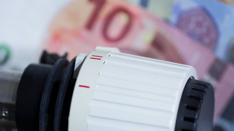 Ein Heizungsregler vor unscharfen Eurobanknoten, symbolisiert Energiekosten.