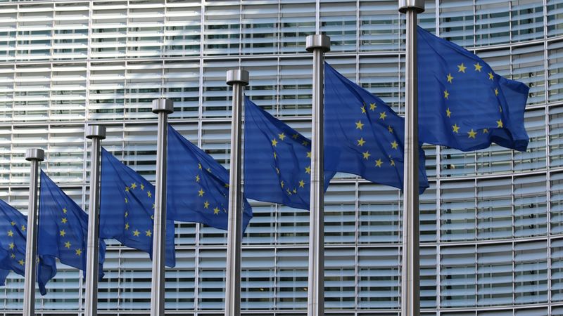 Mehrere Flaggen der Europäischen Union wehen vor einem modernen Gebäude.