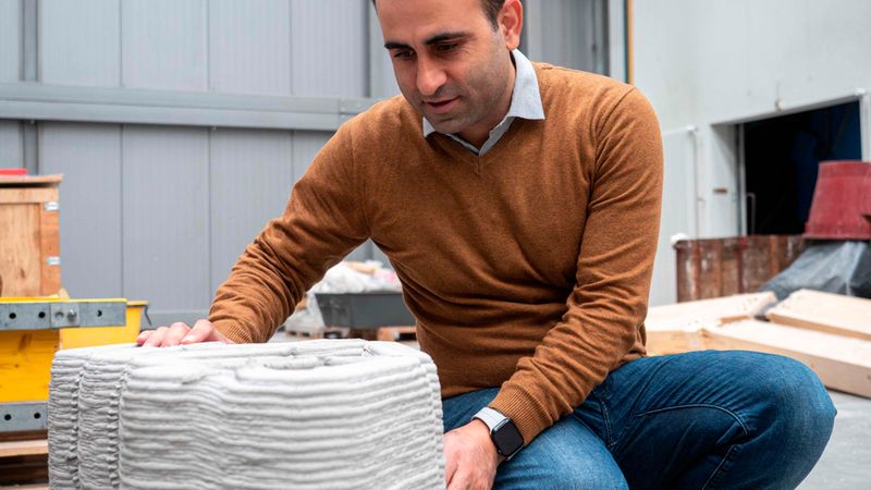 Ein Mann betrachtet einen 3D-gedruckten Betonblock in einer Werkstatt.