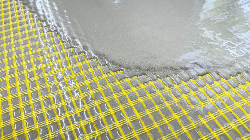 Flüssiger Beton wird auf ein gelbes Glasfasergewebe gegossen, um eine stabile Basis zu schaffen.