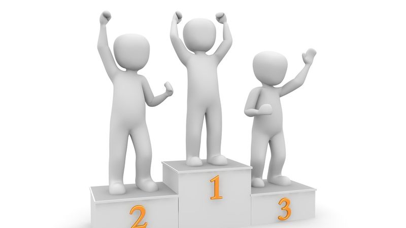 Hauptmotiv: Drei stilisierte 3D-Figuren stehen jubelnd auf einem Siegertreppchen mit den Platzierungen 1, 2 und 3. Das Bild zeigt ein weißes, minimalistisches Podest mit deutlich sichtbaren Zahlen und symbolisiert Wettbewerb, Erfolg und Rangfolge.