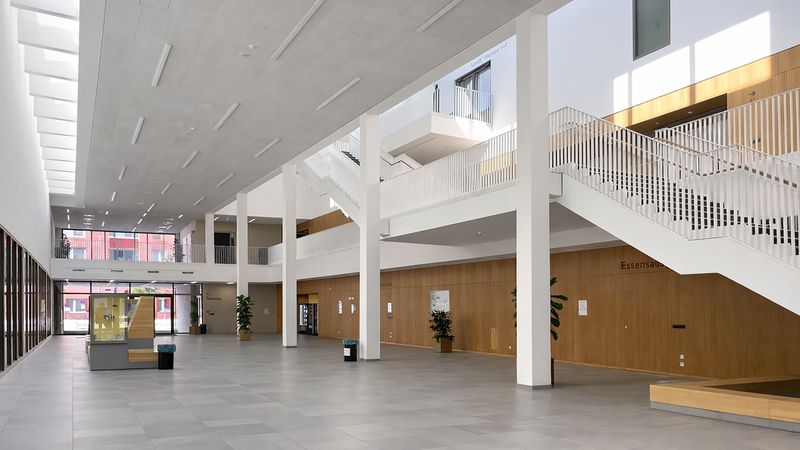 Ein moderner, lichtdurchfluteter Innenraum mit hohen Decken, großen Fenstern und einer breiten Treppe.