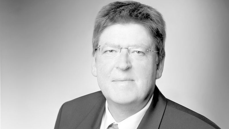 Schwarz-Weiß-Studioporträt eines älteren Mannes in Anzug und Krawatte mit Brille. Kopf- und Schulteraufnahme vor neutralem Hintergrund, seriöser und professioneller Ausdruck. Hauptmotiv: Porträt eines Mannes.