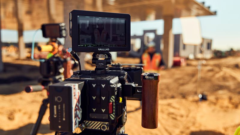 Eine professionelle Filmkamera mit Monitor und Rig im Vordergrund, aufgenommen auf einer sonnigen Baustelle.