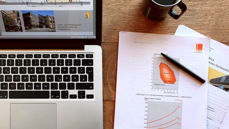 Schreibtisch mit Laptop, Kaffeetasse und Dokumenten.