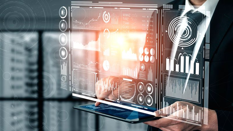 Hauptmotiv: Eine Geschäftsperson hält ein Tablet, aus dem transparente, holografische Dashboards mit Diagrammen, Grafiken und Statistiken aufsteigen. Das Bild zeigt moderne Datenvisualisierung und Business-Analytics in einem Büroumfeld, betont Interaktion mit Touchscreen, Finanzdaten und digitale Visualisierungstechnologien.