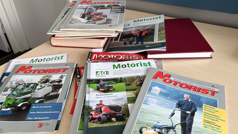 Eine Auswahl verschiedener Ausgaben der Fachzeitschrift Motorist, die auf einem Holztisch liegen. Die Cover zeigen unterschiedliche Garten- und Landschaftspflegegeräte wie Rasentraktoren und Mäher.