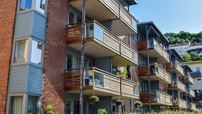 Eine Außenansicht einer modernen Wohnanlage, die durch ihre markante Fassade aus rotem Backstein und stilvollen Holzbalkonen besticht, welche sich über mehrere Etagen erstrecken.
