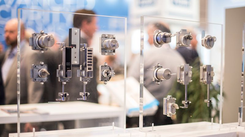 Eine detaillierte Präsentation verschiedener Schließsysteme und Schlösser, die an transparenten Acrylplatten auf einer Fachmesse montiert sind.