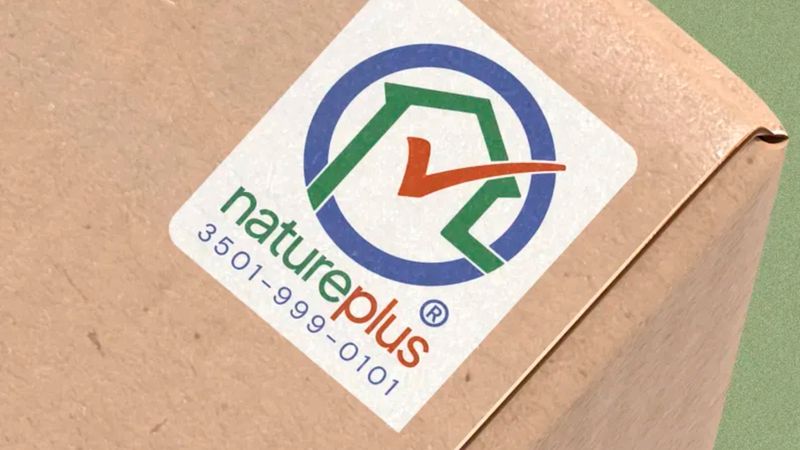 Ein detailliertes Nahaufnahme-Foto des natureplus Gütesiegels, das auf eine braune Kartonverpackung gedruckt ist. Das Logo besteht aus einem blauen Kreis, einem grünen Haus-Symbol und einem orangefarbenen Haken, ergänzt durch die Identifikationsnummer 3501-999-0101.