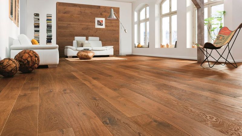 Ein lichtdurchfluteter, moderner Wohnraum mit einem hochwertigen, warmen Eichenparkett-Boden als Hauptmotiv, ergänzt durch weiße Möbel, eine holzverkleidete Wand und eine stilvolle Einrichtung.