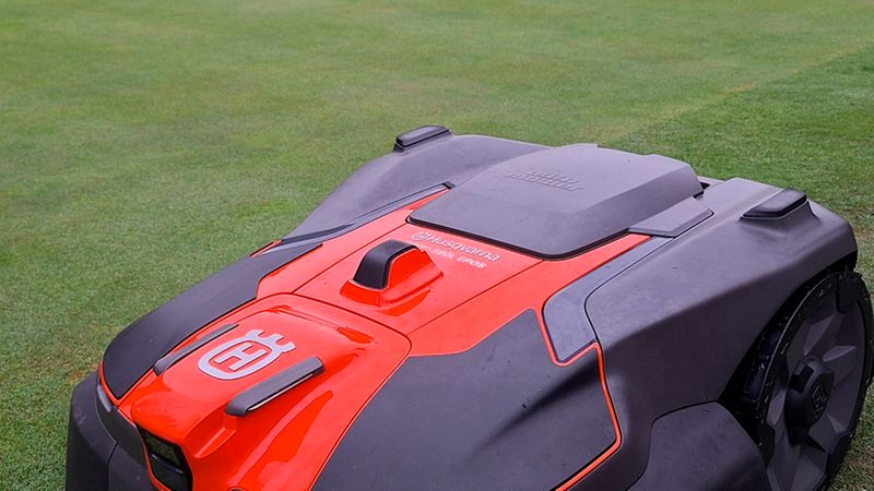 Ein Husqvarna Automower Mähroboter in Orange und Schwarz bei der Arbeit auf einem gepflegten Golfplatz-Grün unter bewölktem Himmel.