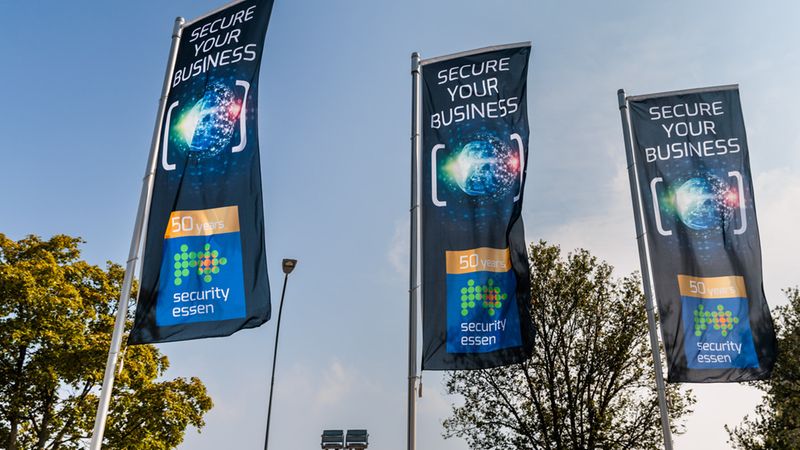 Drei identische Werbeflaggen der Messe Security Essen vor einem blauen Himmel, die das Jubiläum 50 Jahre Security Essen mit dem Slogan Secure Your Business bewerben.