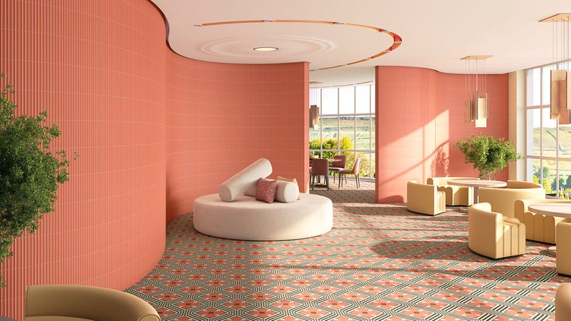 Ein stilvoll gestalteter Lounge-Bereich mit markanten korallenroten, gerippten Wänden und einem auffälligen Bodenbelag mit geometrischem Muster. Der Raum ist mit beigen, geschwungenen Loungesesseln und einem runden Polster-Sofa ausgestattet, ergänzt durch große Fenster mit Blick auf eine grüne Landschaft.