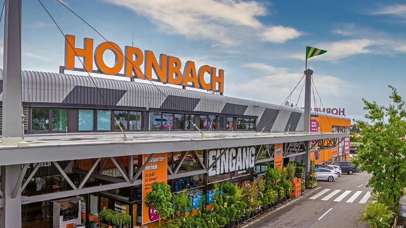 Der Eingang eines Hornbach Baumarkts mit großen Schildern und Pflanzen im Vordergrund.