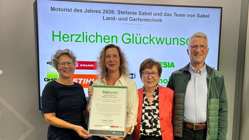 Vier Personen stehen lächelnd auf einer Bühne vor einem Bildschirm mit der Aufschrift 'Motorist des Jahres 2026' und halten eine offizielle Auszeichnungsurkunde für Stefanie Sabel und das Team von Sabel Land- und Gartentechnik in die Kamera.