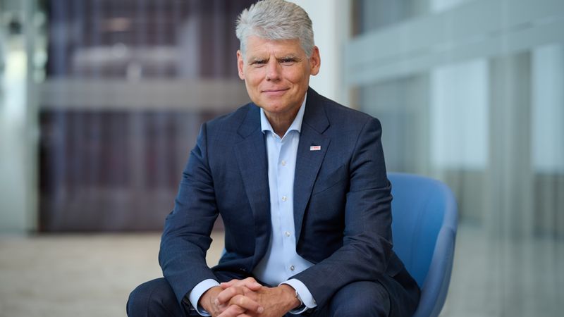 Ein professionelles Porträt von Dr. Stefan Hartung, dem Vorsitzenden der Geschäftsführung der Robert Bosch GmbH, der in einem blauen Anzug auf einem Stuhl in einem modernen Büroumfeld sitzt.
