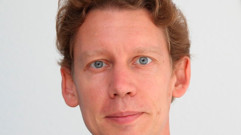Ein professionelles Porträt eines hellhäutigen Mannes mit kurzem, braunem Haar, der ein hellblaues Hemd und ein dunkelblaues Sakko trägt und freundlich in die Kamera blickt.