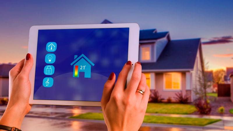 Eine Person steuert mit einem Tablet ein Smart Home System, wobei auf dem Bildschirm verschiedene Funktionen wie Temperaturregelung, Beleuchtung und Sicherheit angezeigt werden, während im Hintergrund ein Haus in der Dämmerung zu sehen ist.