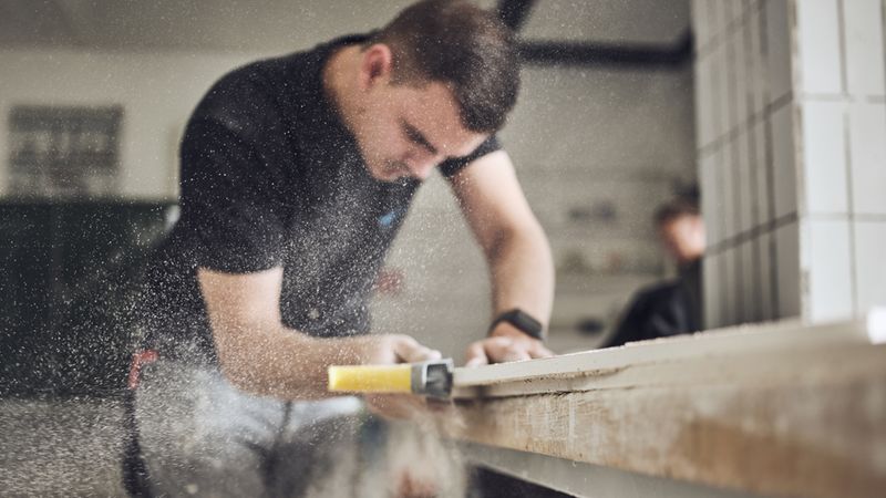 Ein Handwerker bei der Holzbearbeitung in einer Werkstatt, während feiner Holzstaub durch die Luft wirbelt.