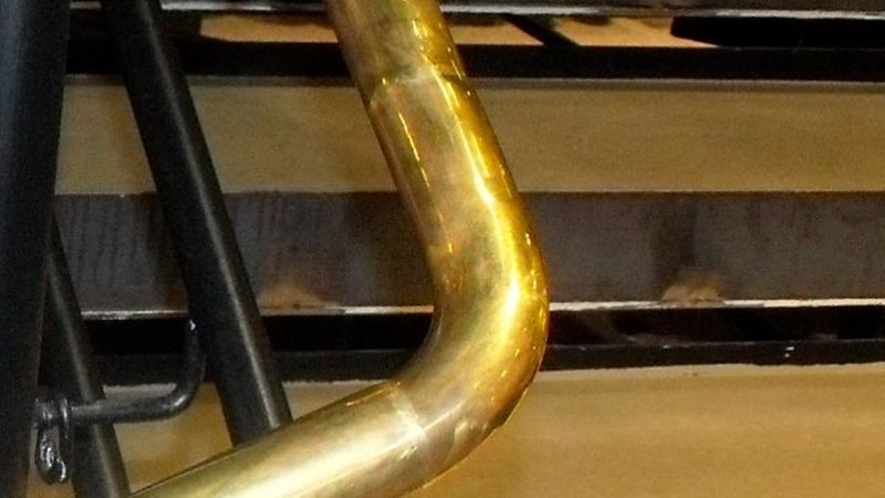 Nahaufnahme eines glänzenden, goldenen Metallhandlaufs, der sich an einer Treppe mit dunklen Stufen entlangzieht.