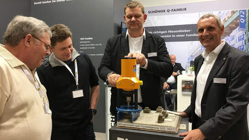 Zwei Kunden lassen sich bei Schönox Haftzugsfestigkeitsmessung demonstrieren: an der Zugprüfmaschine Stefan Marx, Anwendungstechniker Fliesentechnik, und rechts neben ihm Verkaufsleiter Marco Banjamins.
