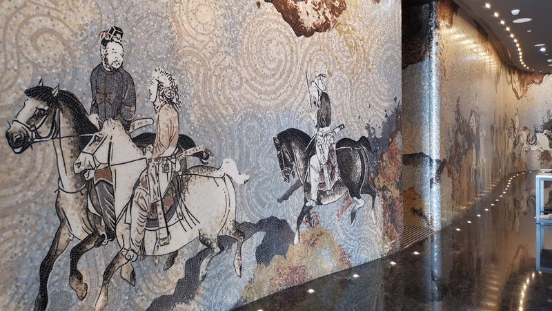 Der König und sein Gefolge zu Pferde: Die historische Szene aus der Zeit der Seidenstraße, die dem Mittelalter entspricht. Das Mosaik reproduziert die reichen Details der Vorlage in Steinchen aus Gold und Muranoglas.