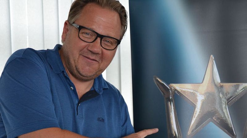 Ein Mann in einem blauen Hemd zeigt auf einen großen Pokal mit einem Stern.