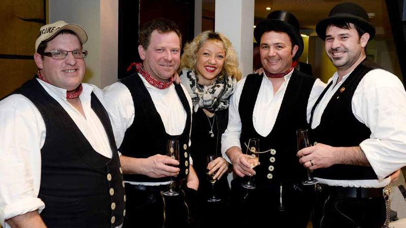 Eine Gruppe von Menschen in traditioneller Kleidung posiert fröhlich mit Getränken in der Hand.