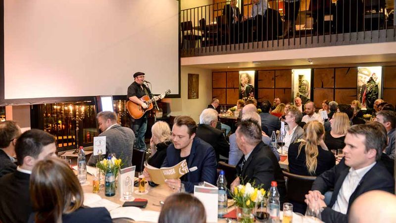 Ein Musiker tritt mit seiner Gitarre auf einem Galaabend vor einem Publikum auf.