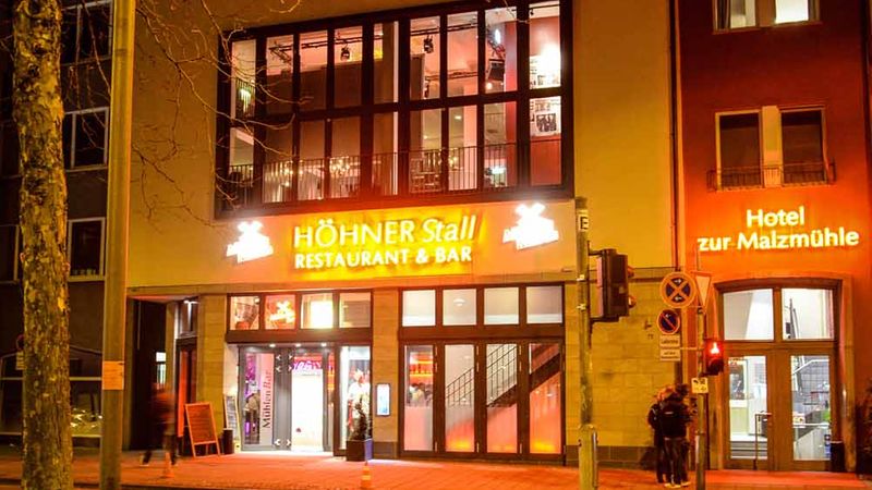 Das Bild zeigt das Restaurant und Bar "Höhner Stall" bei Nacht, beleuchtet mit warmem Licht.