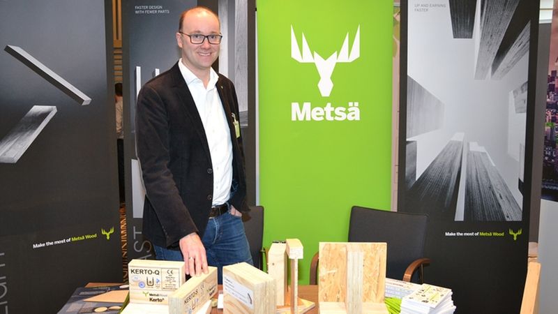 Ein Mann steht an einem Messestand, der Holzprodukte von Metsä präsentiert.