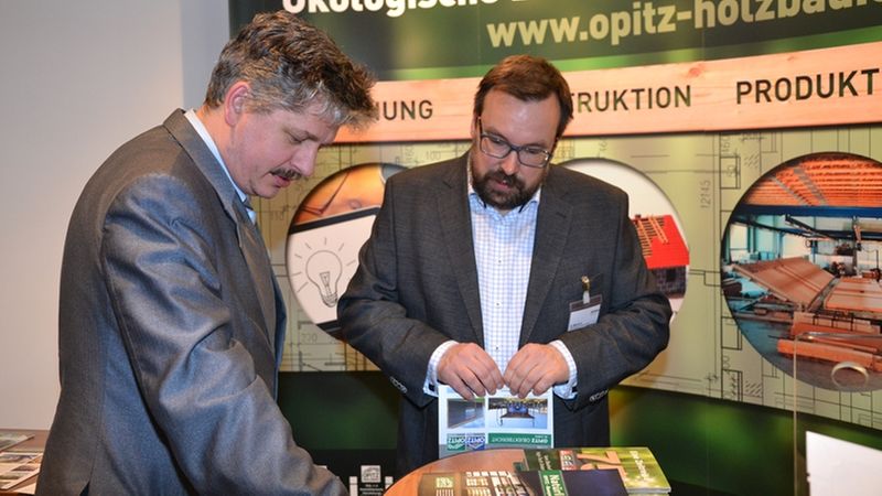 Zwei Männer führen ein Gespräch an einem Messestand über ökologische Bausysteme.