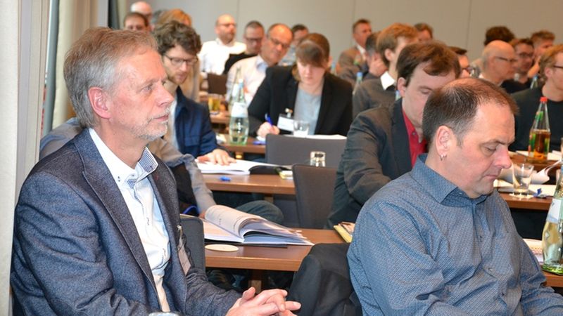 Teilnehmer einer Konferenz sitzen aufmerksam im Publikum und machen sich Notizen.