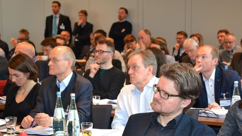 Eine Gruppe von Menschen sitzt aufmerksam in einem Konferenzraum und hört einem Vortrag zu.