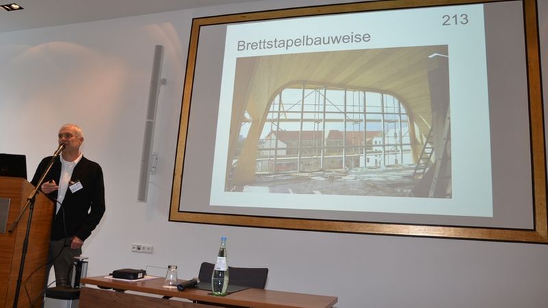 Ein Vortrag über die Brettstapelbauweise mit einem Bild einer Baustelle auf der Leinwand.