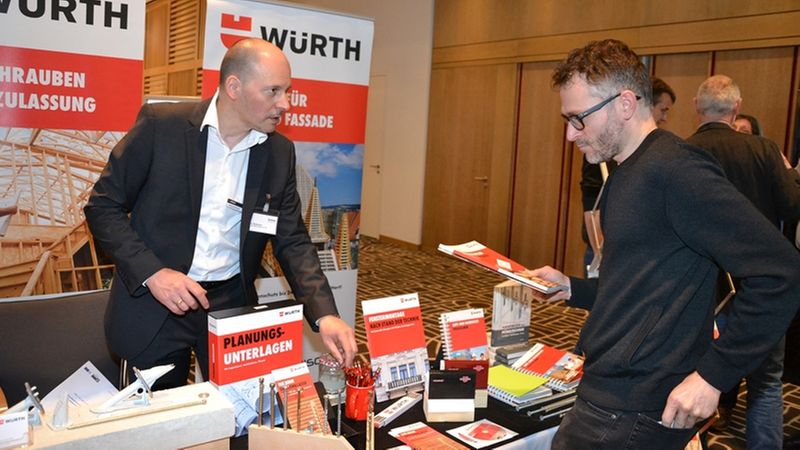Ein Messe-Stand von Würth mit einem Mitarbeiter, der einem Besucher Informationsmaterial überreicht.