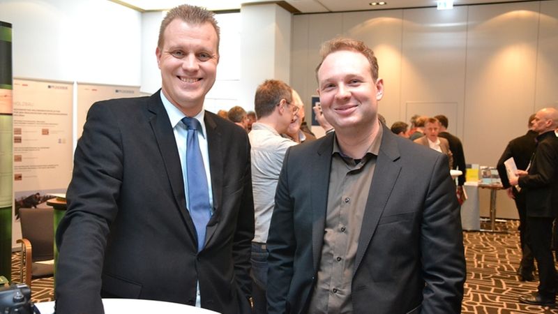 Zwei Männer in Anzügen bei einem Geschäftstreffen in einem Konferenzraum.