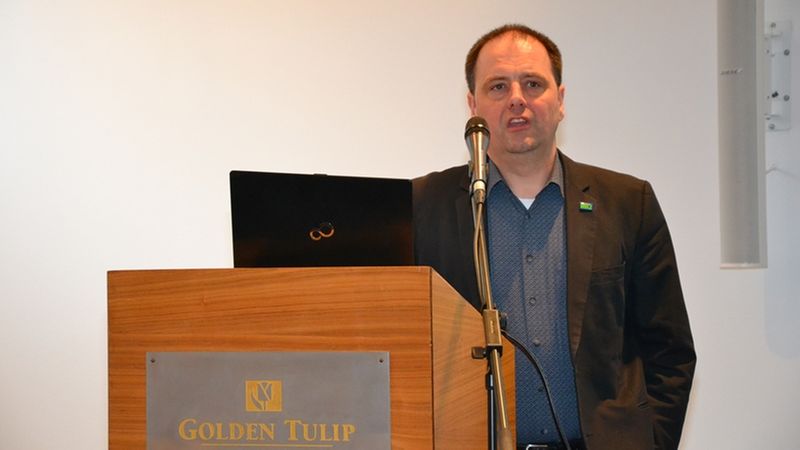 Ein Mann steht an einem Rednerpult und hält eine Präsentation in einem Konferenzraum.