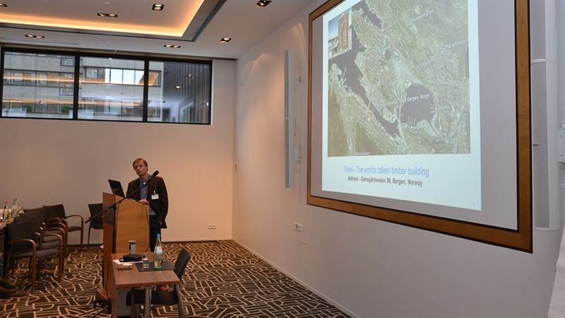 Ein Vortragender hält eine Präsentation in einem modernen Konferenzraum mit einem großen Bildschirm.