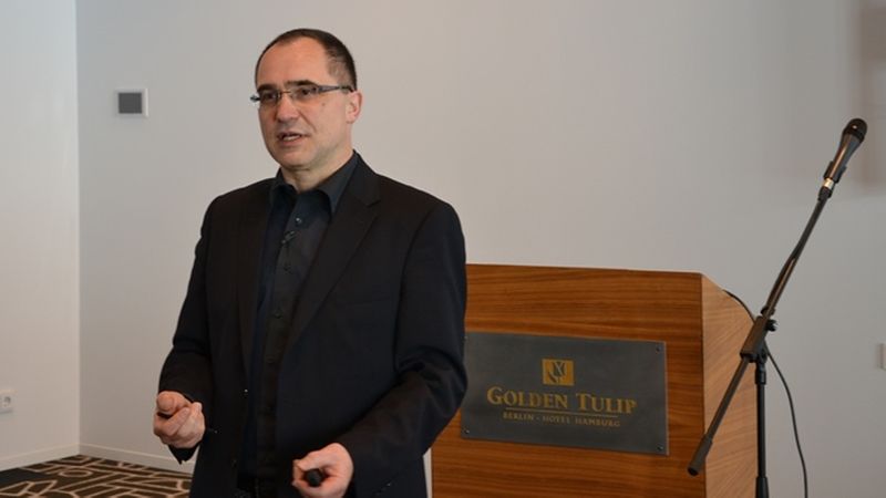 Ein Mann hält einen Vortrag in einem Konferenzraum neben einem Rednerpult.