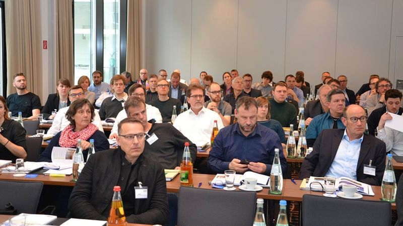 Eine Gruppe von Konferenzteilnehmern sitzt aufmerksam in einem modernen Konferenzraum.