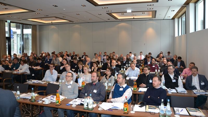 Ein Konferenzraum voller Teilnehmer, die aufmerksam einem Vortrag folgen.